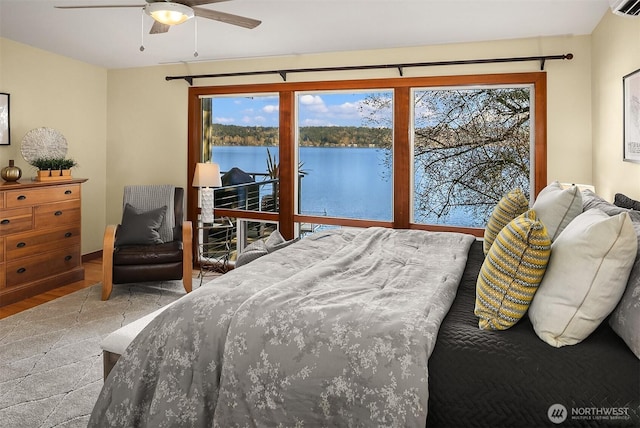 bedroom with a ceiling fan, access to exterior, wood finished floors, and a water view