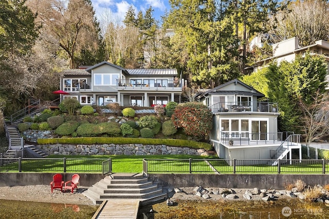 rear view of property featuring a balcony, stairway, a standing seam roof, a yard, and fence private yard