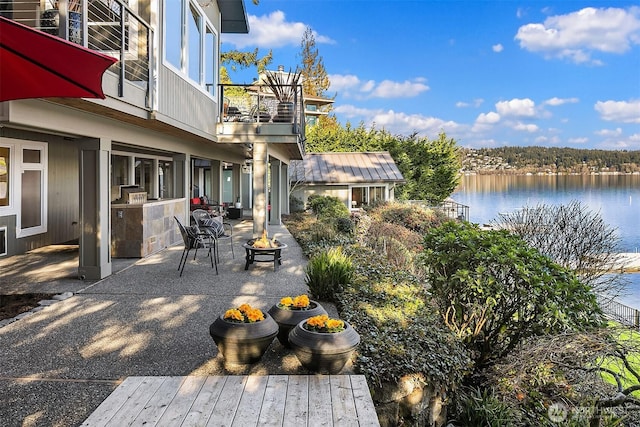 view of patio with a water view, a fire pit, and a balcony