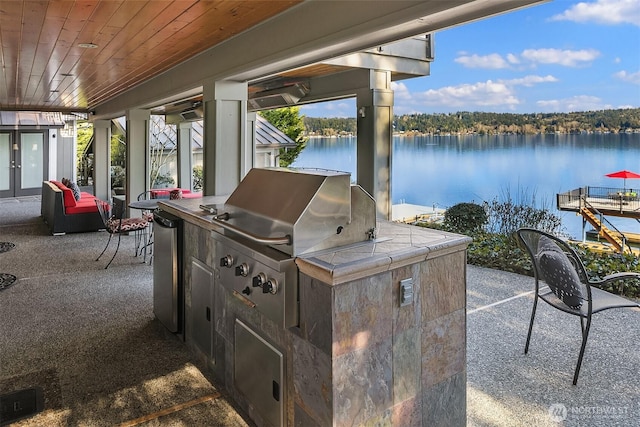 view of patio with french doors, a water view, area for grilling, and an outdoor kitchen