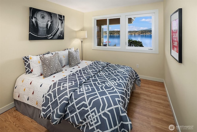 bedroom featuring wood finished floors, a water view, and baseboards