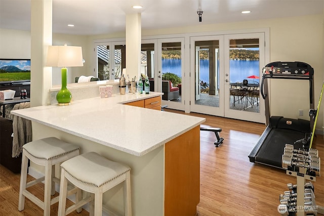 kitchen featuring light wood finished floors, a peninsula, recessed lighting, french doors, and a kitchen breakfast bar