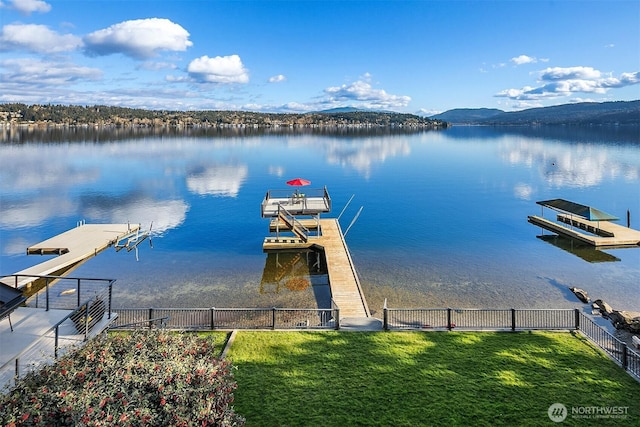 view of dock with a yard, a water and mountain view, and fence