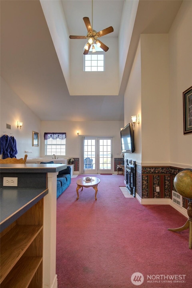 carpeted living area with a high ceiling, plenty of natural light, a fireplace with flush hearth, and a ceiling fan