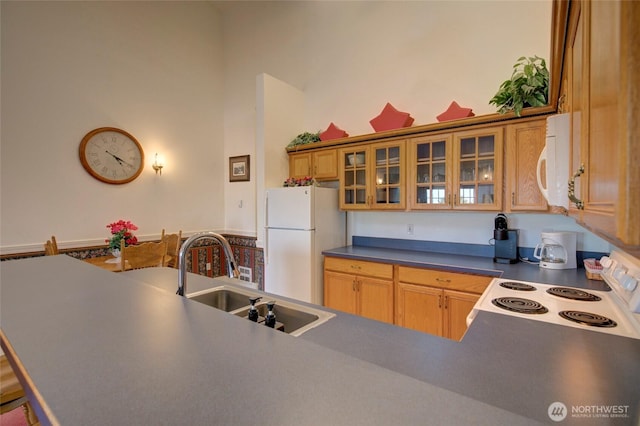 kitchen with white appliances, dark countertops, a towering ceiling, glass insert cabinets, and a sink