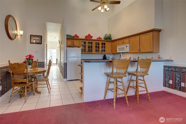 kitchen with white appliances, light colored carpet, a towering ceiling, brown cabinets, and a peninsula