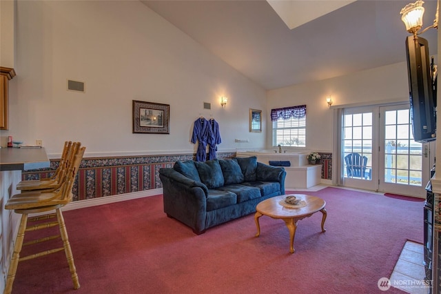 carpeted living room featuring a wainscoted wall, visible vents, and high vaulted ceiling