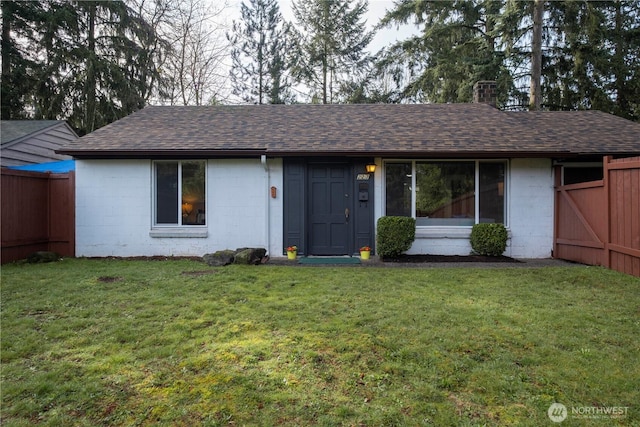 ranch-style home featuring concrete block siding, a shingled roof, a front yard, and fence