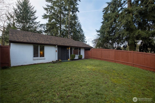 view of front of home featuring roof with shingles, concrete block siding, a fenced backyard, and a front lawn