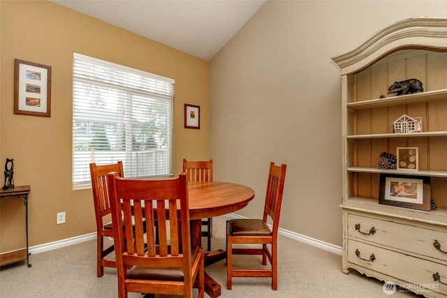 dining room with vaulted ceiling, baseboards, and light carpet