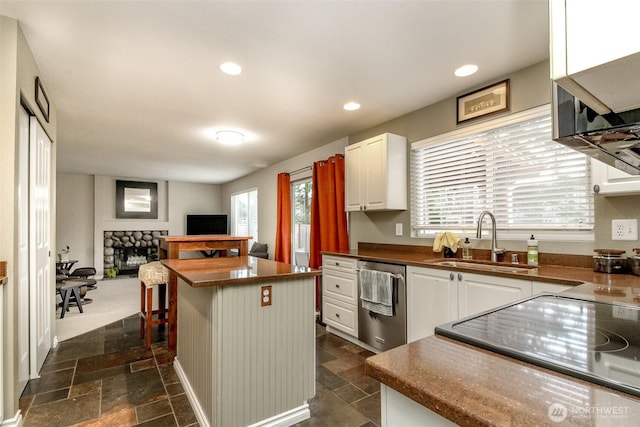 kitchen with a sink, stainless steel dishwasher, stone tile flooring, white cabinetry, and a fireplace