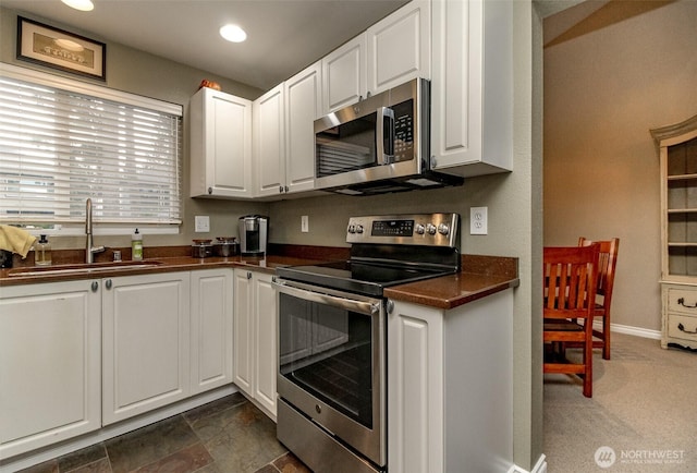 kitchen featuring dark countertops, white cabinetry, stainless steel appliances, and a sink