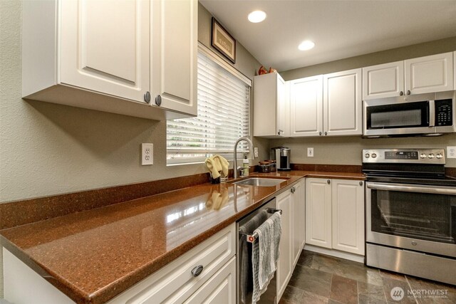 kitchen with a sink, white cabinets, appliances with stainless steel finishes, stone finish flooring, and dark countertops