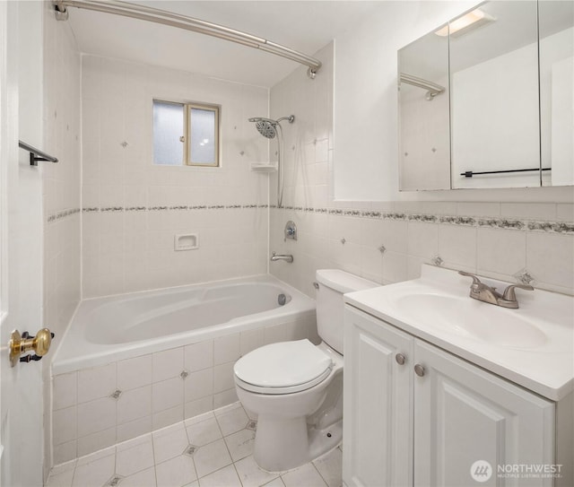 bathroom featuring toilet, tile patterned flooring, tiled shower / bath, vanity, and tile walls