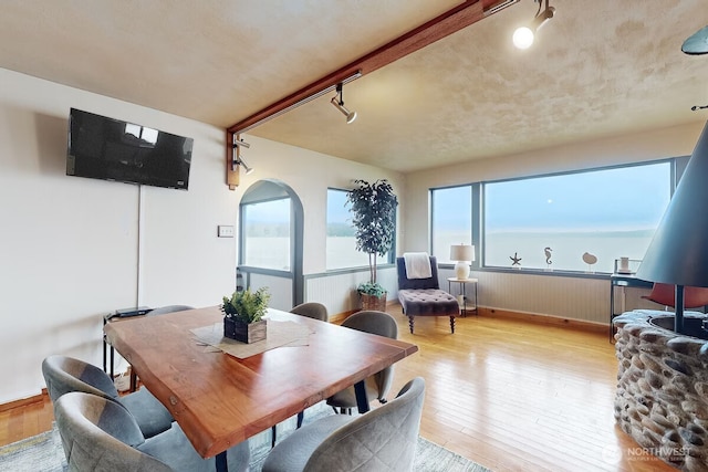 dining area with light wood finished floors, arched walkways, and rail lighting