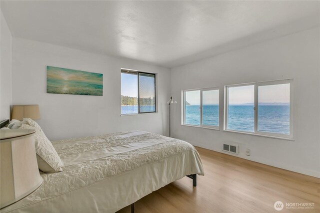 bedroom with visible vents, a water view, and wood finished floors