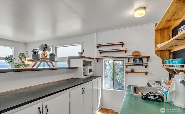 kitchen featuring white microwave, a healthy amount of sunlight, white cabinets, and open shelves