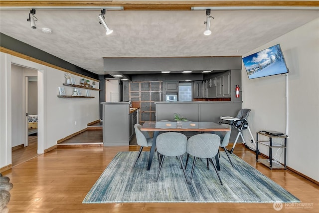 dining area featuring rail lighting, baseboards, and light wood-style floors