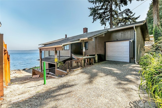 view of front of house featuring an attached garage, a chimney, driveway, and a water view