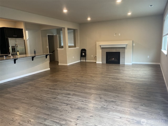 unfurnished living room with dark wood-style flooring, recessed lighting, a tile fireplace, and baseboards