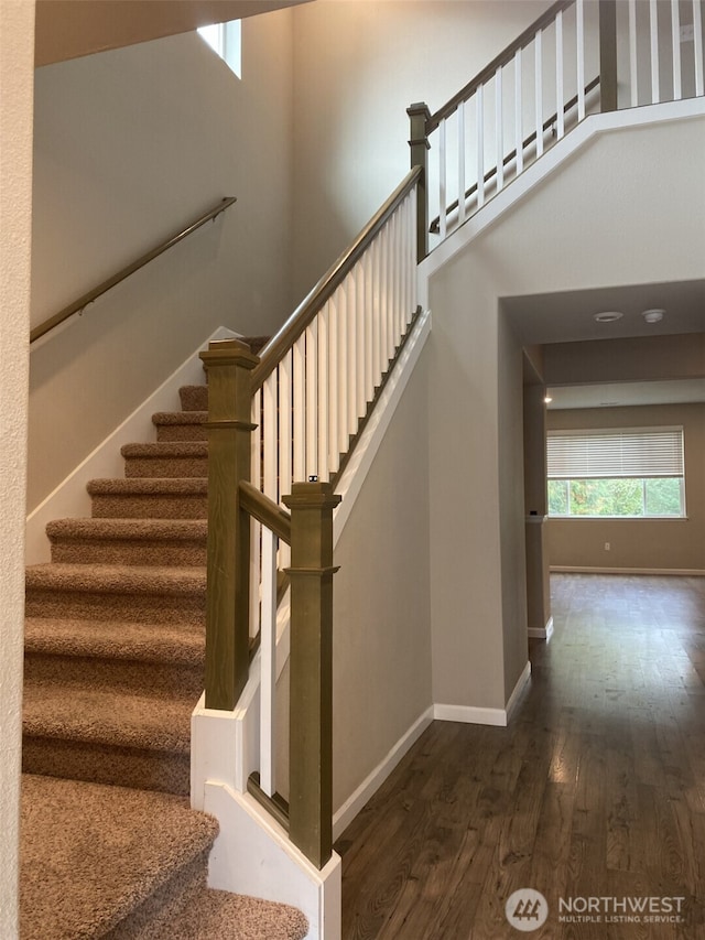 stairway featuring a towering ceiling, baseboards, and wood finished floors