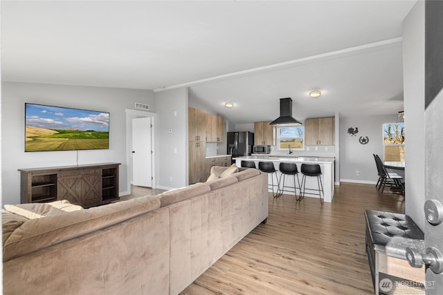 living room featuring vaulted ceiling, light wood-type flooring, visible vents, and baseboards