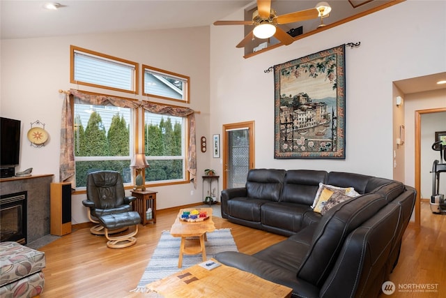 living area with high vaulted ceiling, a tile fireplace, wood finished floors, and a ceiling fan