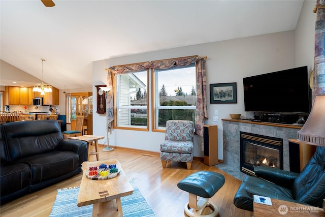 living area with a chandelier, a fireplace, baseboards, vaulted ceiling, and light wood finished floors