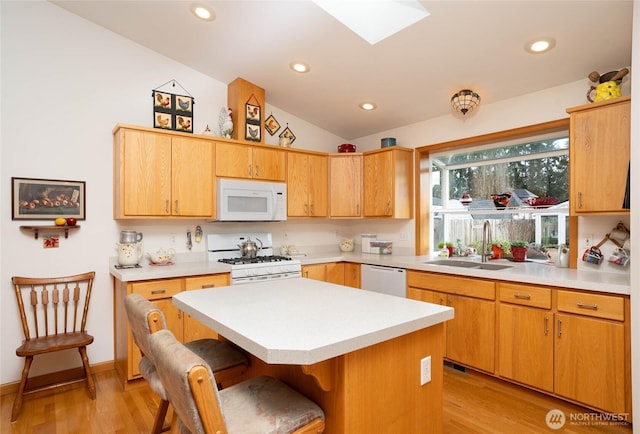 kitchen with white appliances, a breakfast bar, a sink, light countertops, and lofted ceiling with skylight