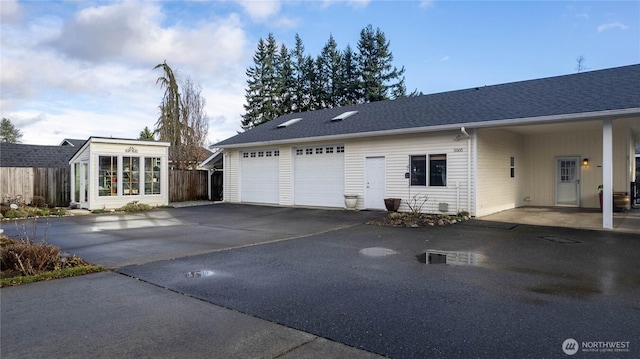 view of side of home featuring a garage, roof with shingles, fence, and driveway