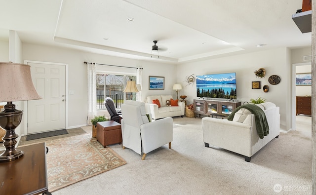 living area with ceiling fan, a tray ceiling, carpet, and baseboards