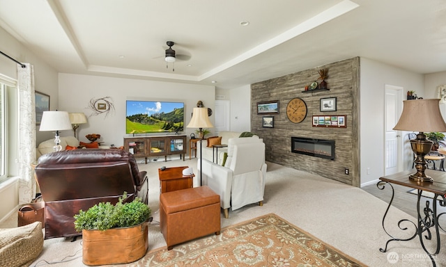 carpeted living room with a tray ceiling, a large fireplace, ceiling fan, and baseboards