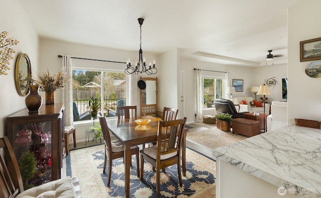 dining room featuring ceiling fan with notable chandelier and baseboards