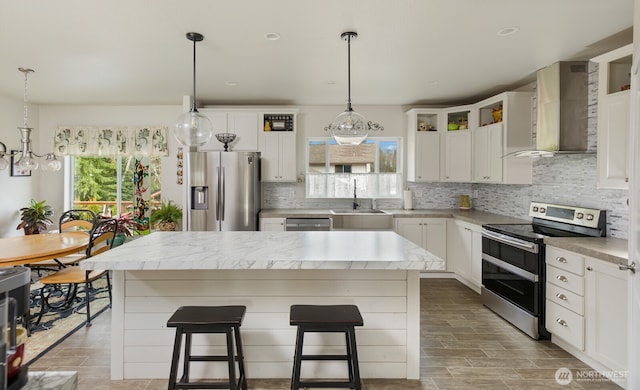 kitchen featuring wall chimney exhaust hood, appliances with stainless steel finishes, a sink, light countertops, and backsplash