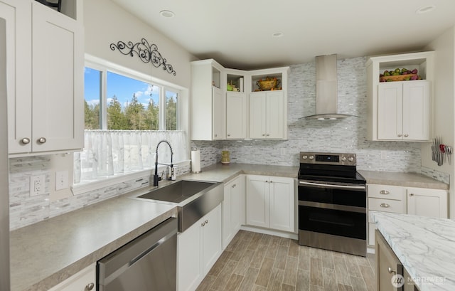 kitchen featuring stainless steel appliances, light countertops, wall chimney range hood, open shelves, and a sink