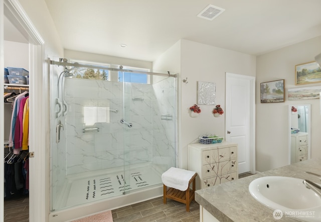 full bathroom with wood finish floors, a marble finish shower, visible vents, a spacious closet, and vanity