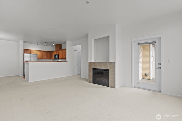 unfurnished living room with baseboards, light colored carpet, and a tiled fireplace