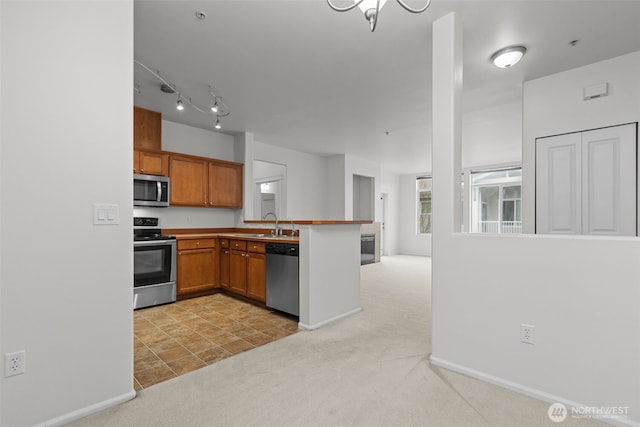 kitchen featuring brown cabinetry, a peninsula, appliances with stainless steel finishes, light colored carpet, and open floor plan