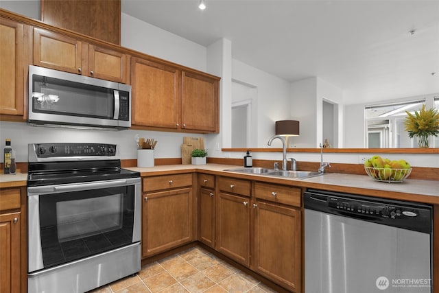 kitchen with light tile patterned floors, a sink, stainless steel appliances, light countertops, and brown cabinets