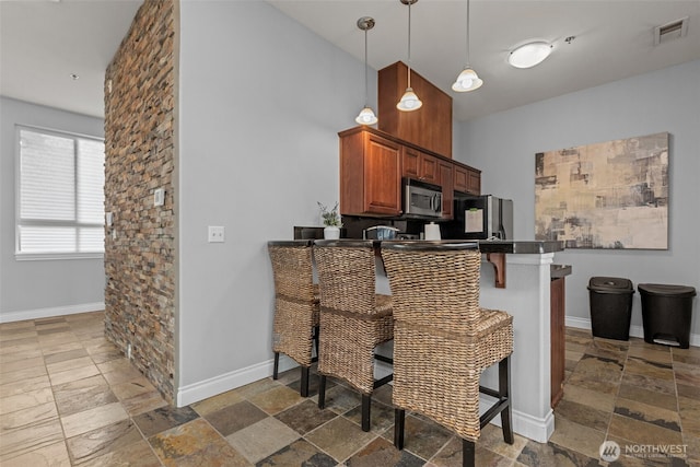 kitchen with visible vents, baseboards, a breakfast bar area, stone tile floors, and stainless steel appliances