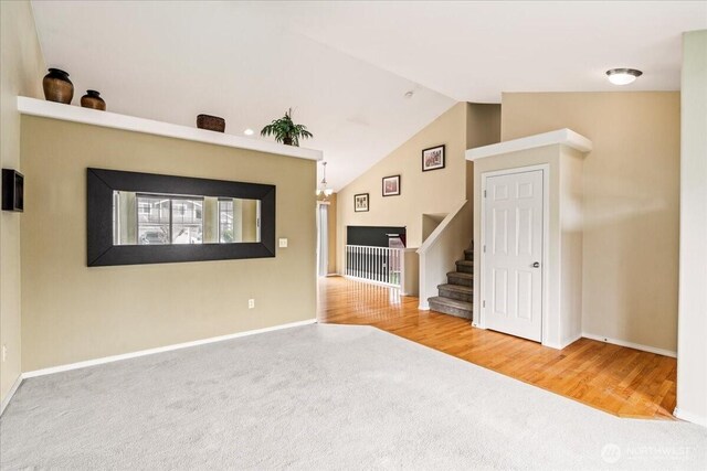 unfurnished living room with baseboards, stairway, vaulted ceiling, carpet floors, and wood finished floors