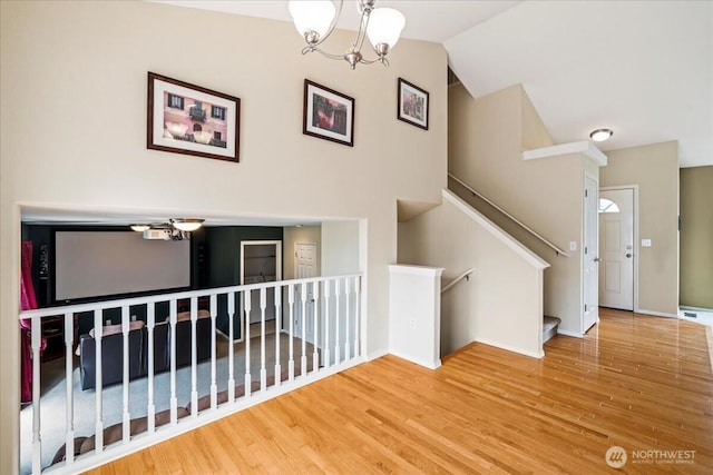 staircase with a notable chandelier, vaulted ceiling, baseboards, and wood finished floors