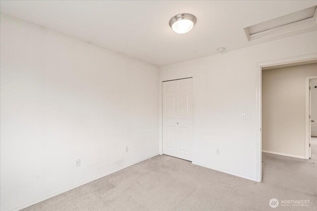 empty room featuring light colored carpet, attic access, and baseboards