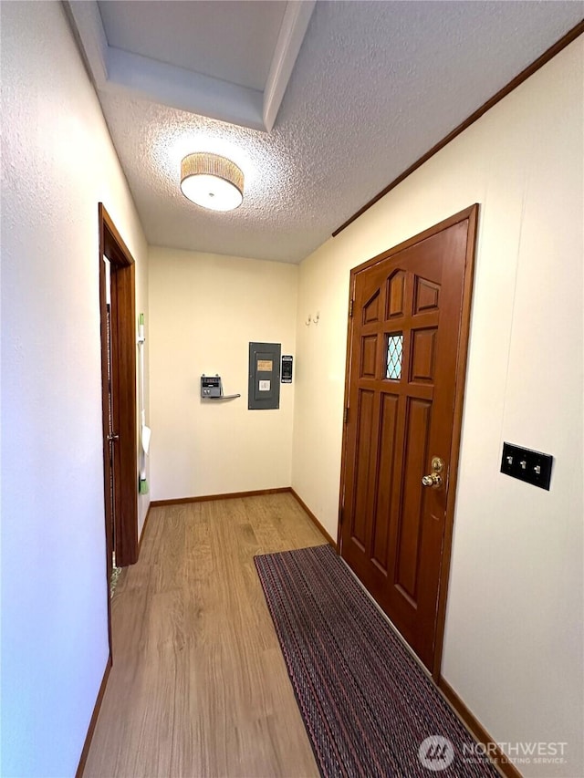 hallway featuring light wood-style flooring, baseboards, and a textured ceiling