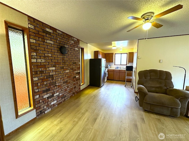 living room with ceiling fan, light wood-type flooring, brick wall, and a textured ceiling