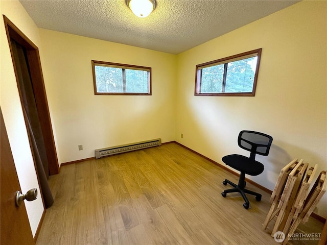 unfurnished office with wood finished floors, baseboards, baseboard heating, and a textured ceiling