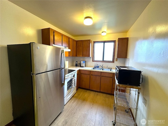 kitchen with white range with electric cooktop, freestanding refrigerator, a sink, black microwave, and brown cabinets