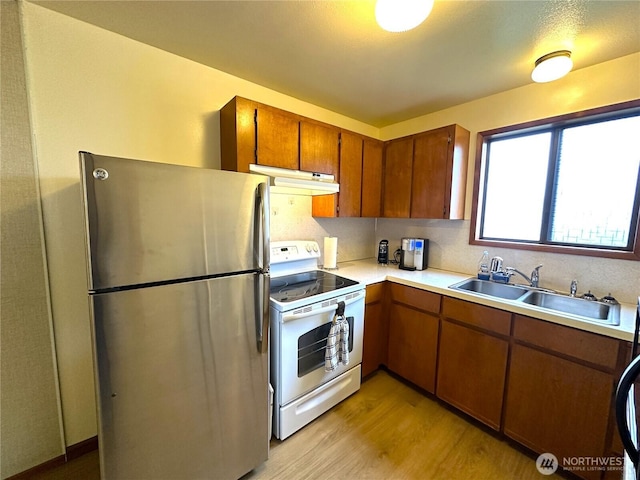 kitchen with white electric range, under cabinet range hood, a sink, freestanding refrigerator, and light countertops