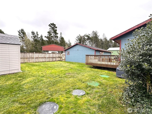 view of yard featuring an outbuilding, a deck, a storage shed, and fence