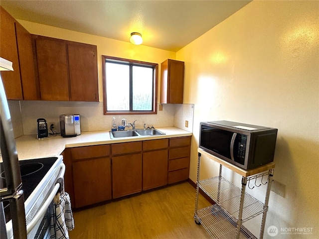 kitchen with light wood finished floors, stainless steel microwave, brown cabinets, electric stove, and a sink